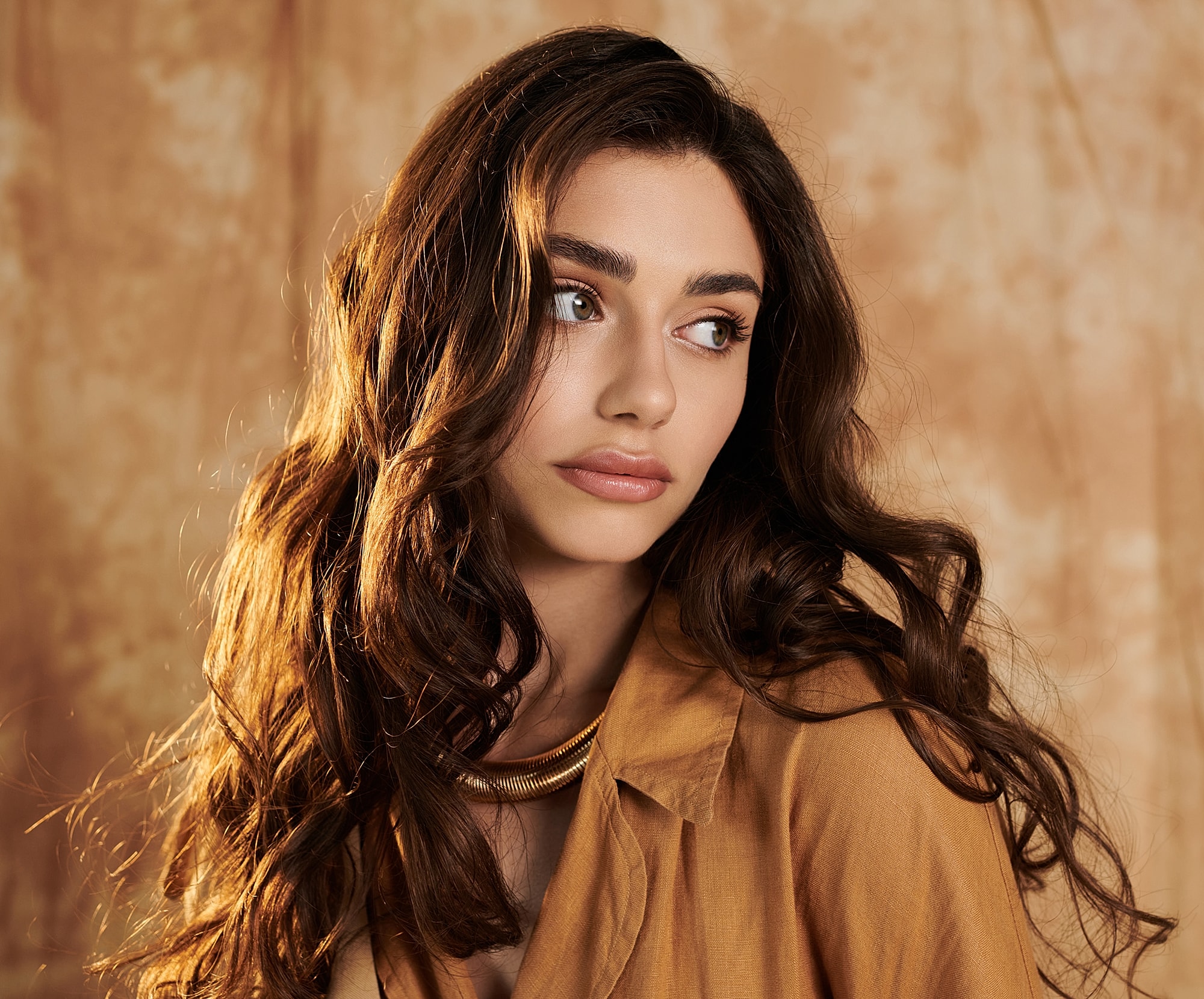 Woman with long, wavy hair and gold necklace.